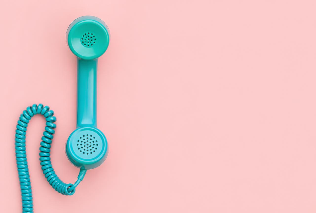 A teal telephone handset resting on a soft pink background